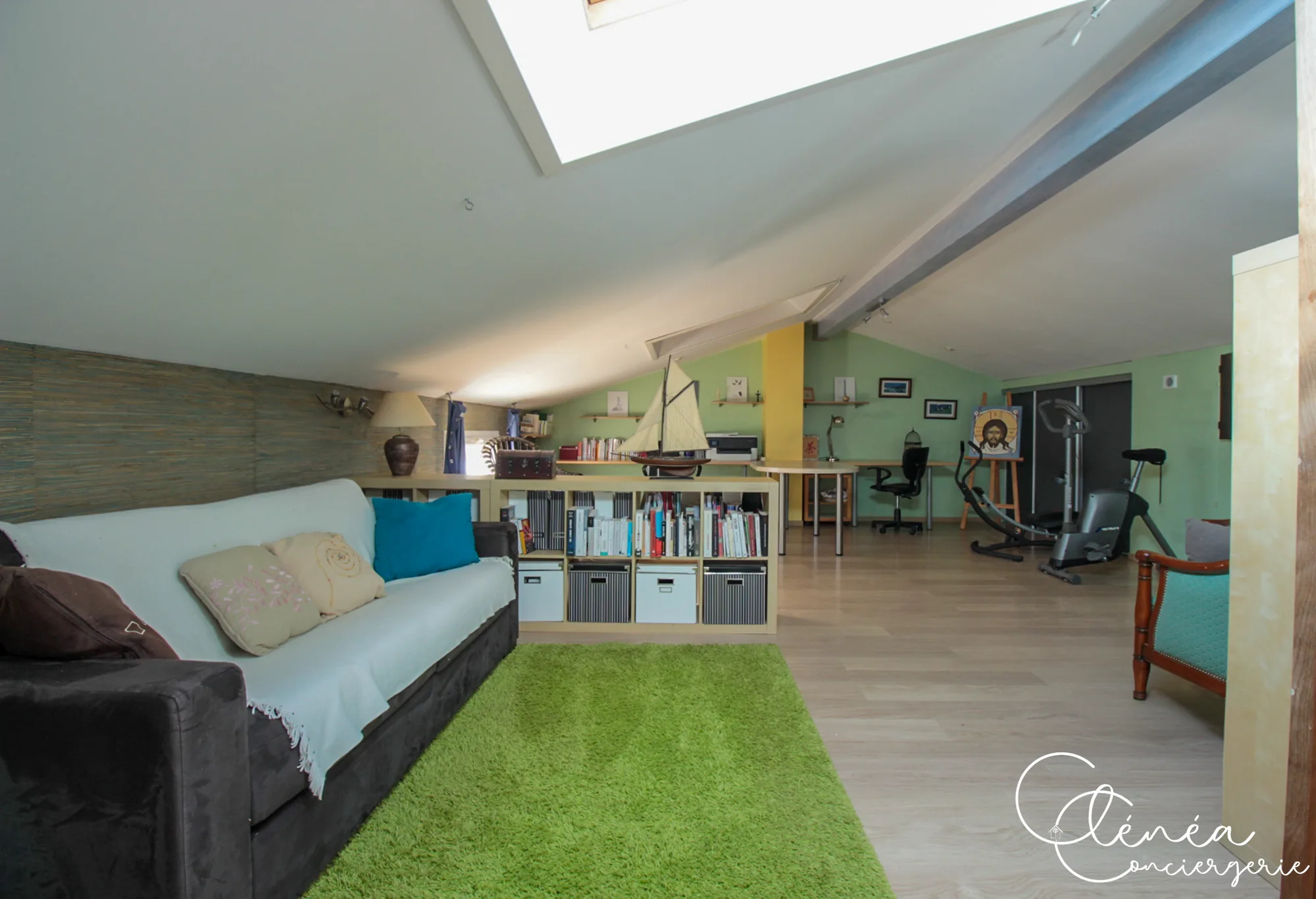 Villa Chanoine — La grande pièce sous les combles avec son canapé, son tapis vert, ses rangements et son coin bureau au fond.