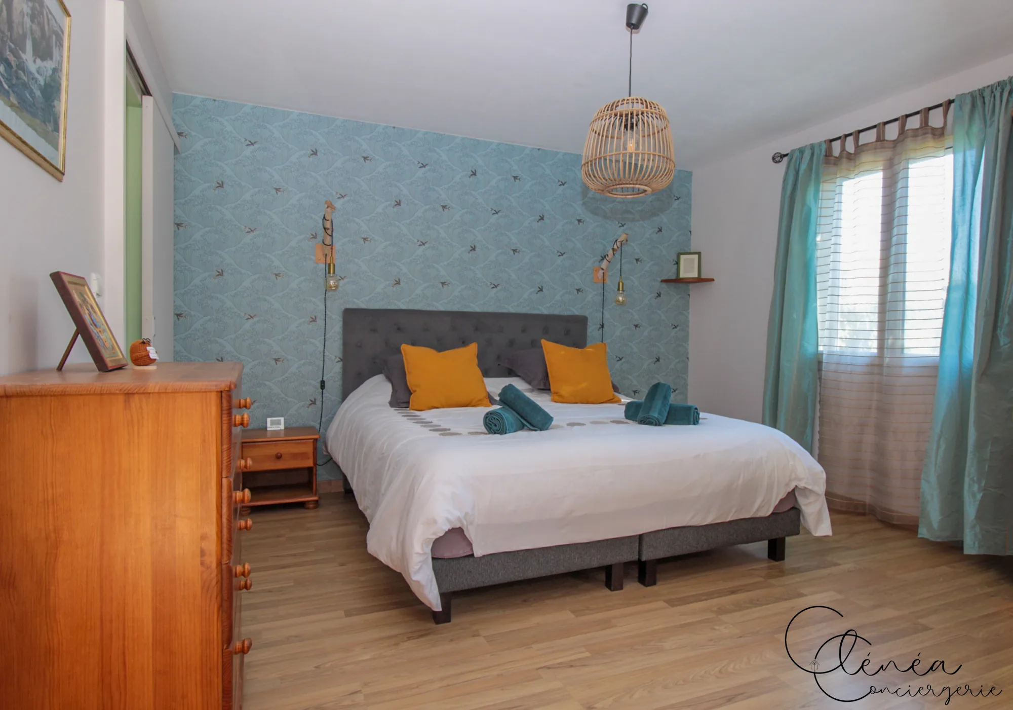 Villa Chanoine — Vue d'ensemble de la chambre 1 avec son lit King size, ses appliques en bois flotté et sa fenêtre habillée de rideaux turquoise.