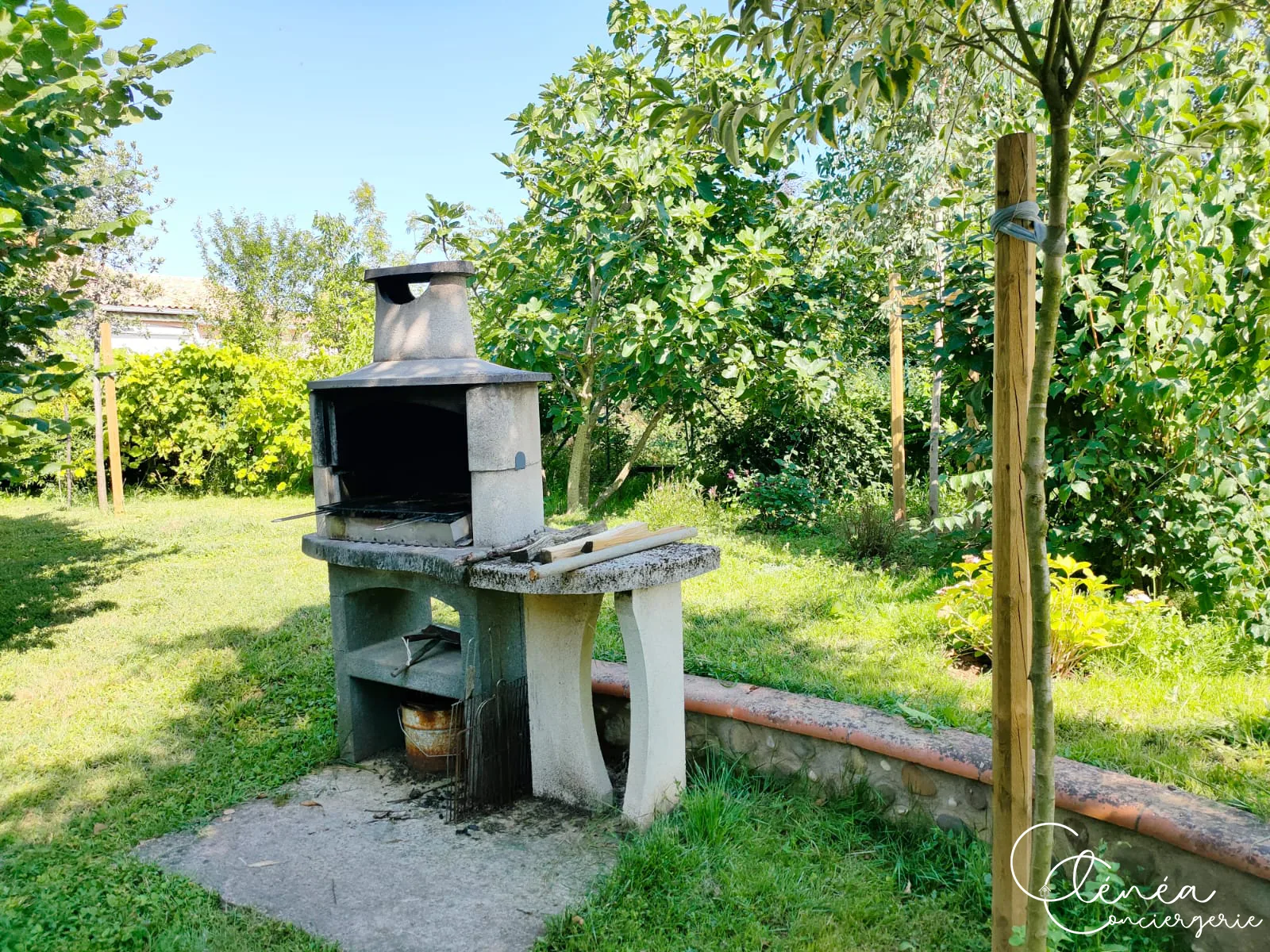 Villa Chanoine — Le barbecue fixe en pierre installé dans le jardin, avec sa réserve de bois.